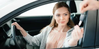 водіння чужим автомобілем у Німеччині 2025. На фото: молода жінка сидить за кермом автомобіля і через вікно їй подають ключ від авто.