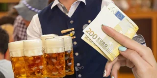 Рекордні ціни на Oktoberfest: за цю страву гості платять 229 євро. На фото: чоловік із кухлями пива, рука яеа тримає купюру 200 євро.